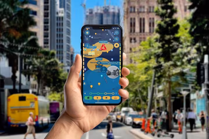 Hand holding a smartphone with Brisbane self-guided dark history walking tour app on a busy city street