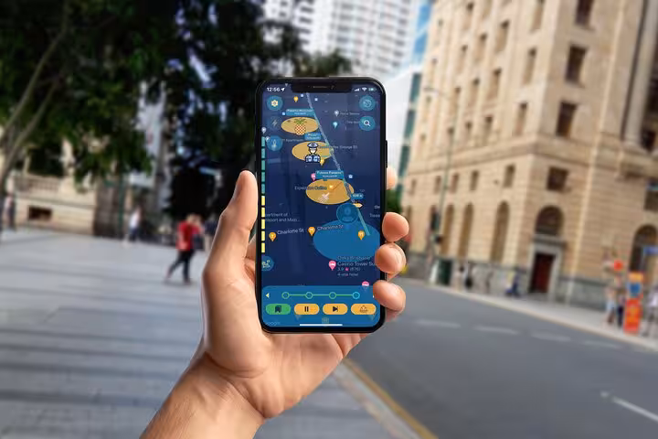 Hand holding a phone displaying Brisbane dark history mystery walking tour map app near historic buildings