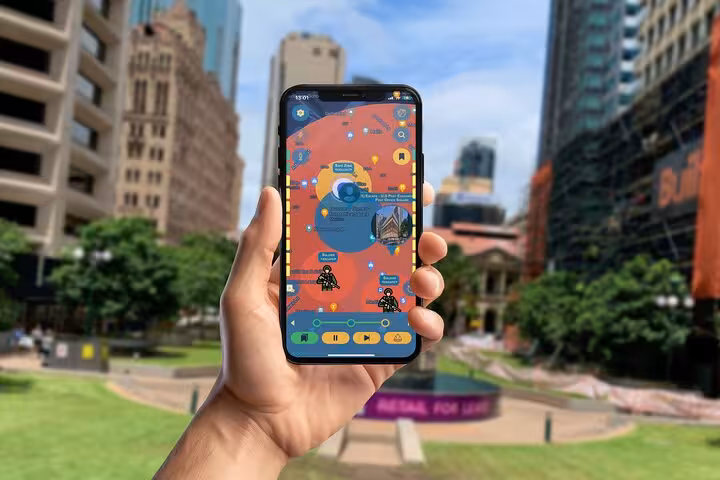 Hand holding phone with interactive Brisbane mystery walking tour app map near historic city landmarks