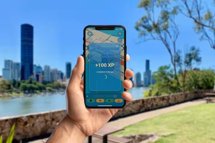 Hand holding smartphone showing +100 XP challenge reward on Brisbane self-guided walking tour app with city skyline
