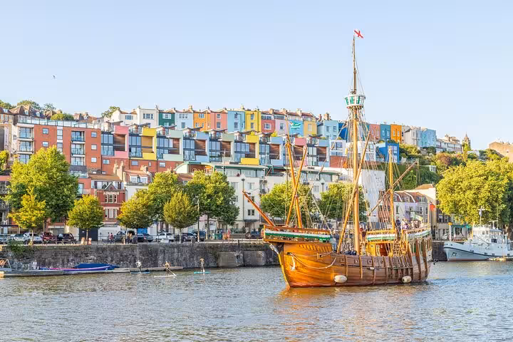 Historic tall ship moored on Bristol Harbour with colourful Cliftonwood houses on hillside behind