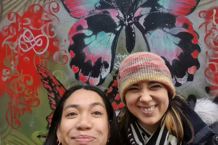 Two women smiling in front of colorful butterfly street art mural in Bristol