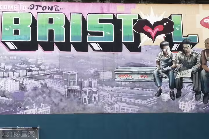 Bristol street art mural with bold graffiti lettering and cityscape, featuring figures sitting above rooftops