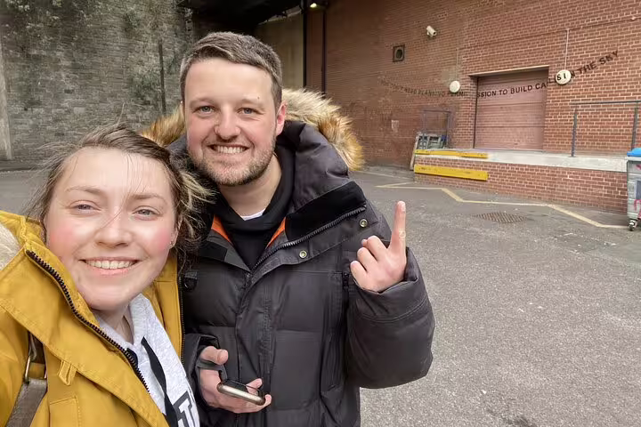 Couple smiling on Bristol street art walking tour near Banksy mural on brick wall