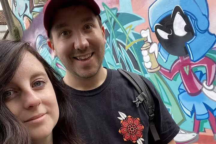 Couple smiling in front of colorful Bristol street art graffiti mural featuring cartoon character