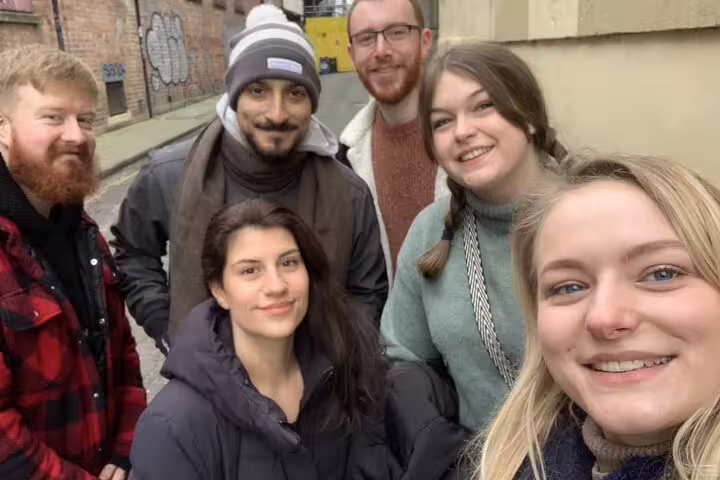 Group of six friends smiling together on a Bristol street art tour in an urban alleyway