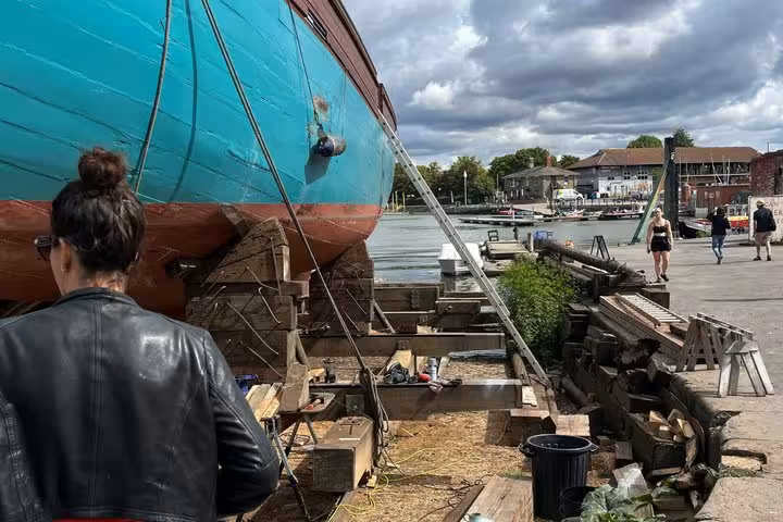 Woman in leather jacket viewing a large turquoise wooden boat in dry dock at Bristol waterfront