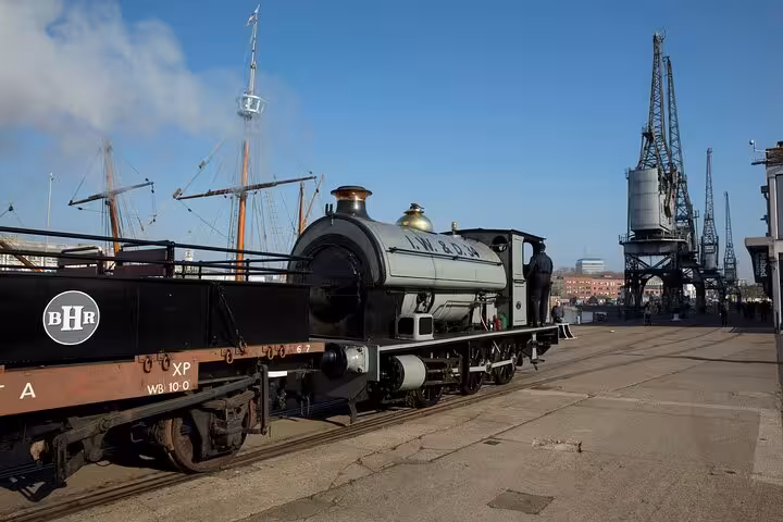Vintage steam locomotive on Bristol waterfront dockside with historic cranes and sailing ship masts in background