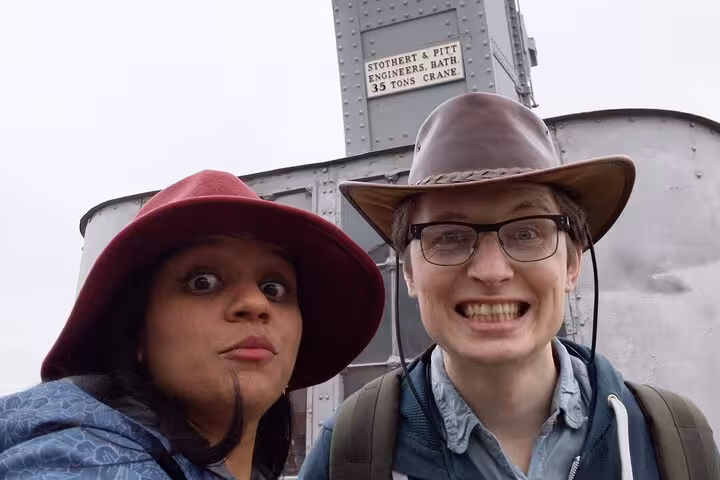 Two smiling tourists wearing hats pose in front of Stothert & Pitt 35-ton crane at Bristol Waterfront