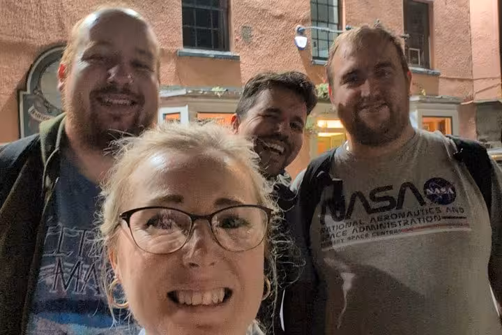 Group of four smiling adults on a night walking tour in an urban street setting