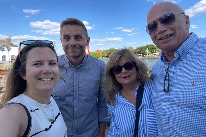Four smiling adults posing for a selfie by a sunny waterfront with blue skies