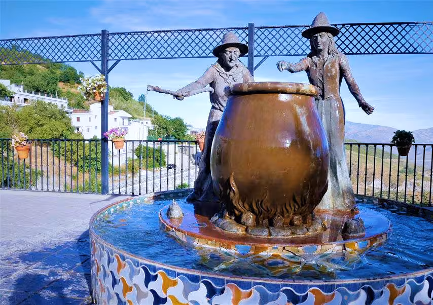 Bronze statues of witches stirring a cauldron in Soportújar, highlighting the village's enchanting theme and scenic views.