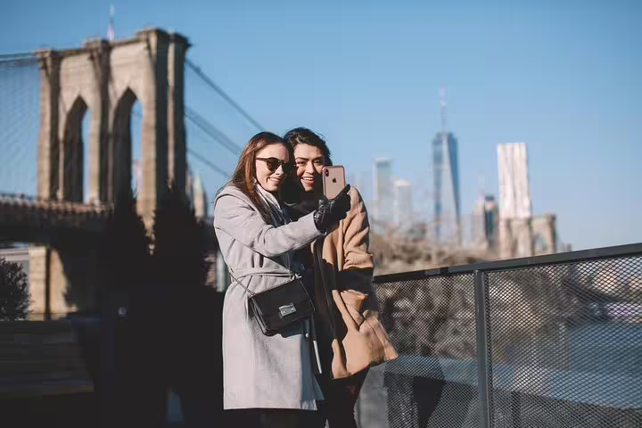 Two friends capture a selfie with the iconic Brooklyn Bridge and Manhattan skyline as backdrop on NYC photography tour.