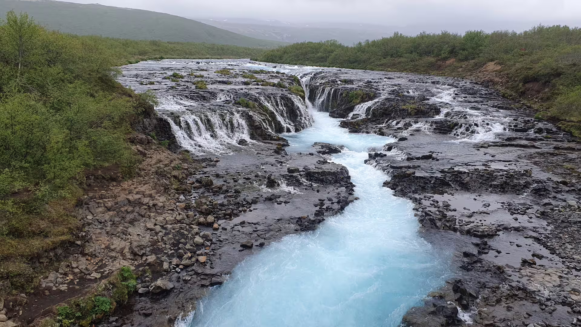 Bruarfoss waterfall with vivid turquoise blue water cascading over dark lava rocks in Iceland