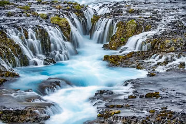 Bruarfoss waterfall with turquoise blue water cascading over mossy lava rocks in Iceland