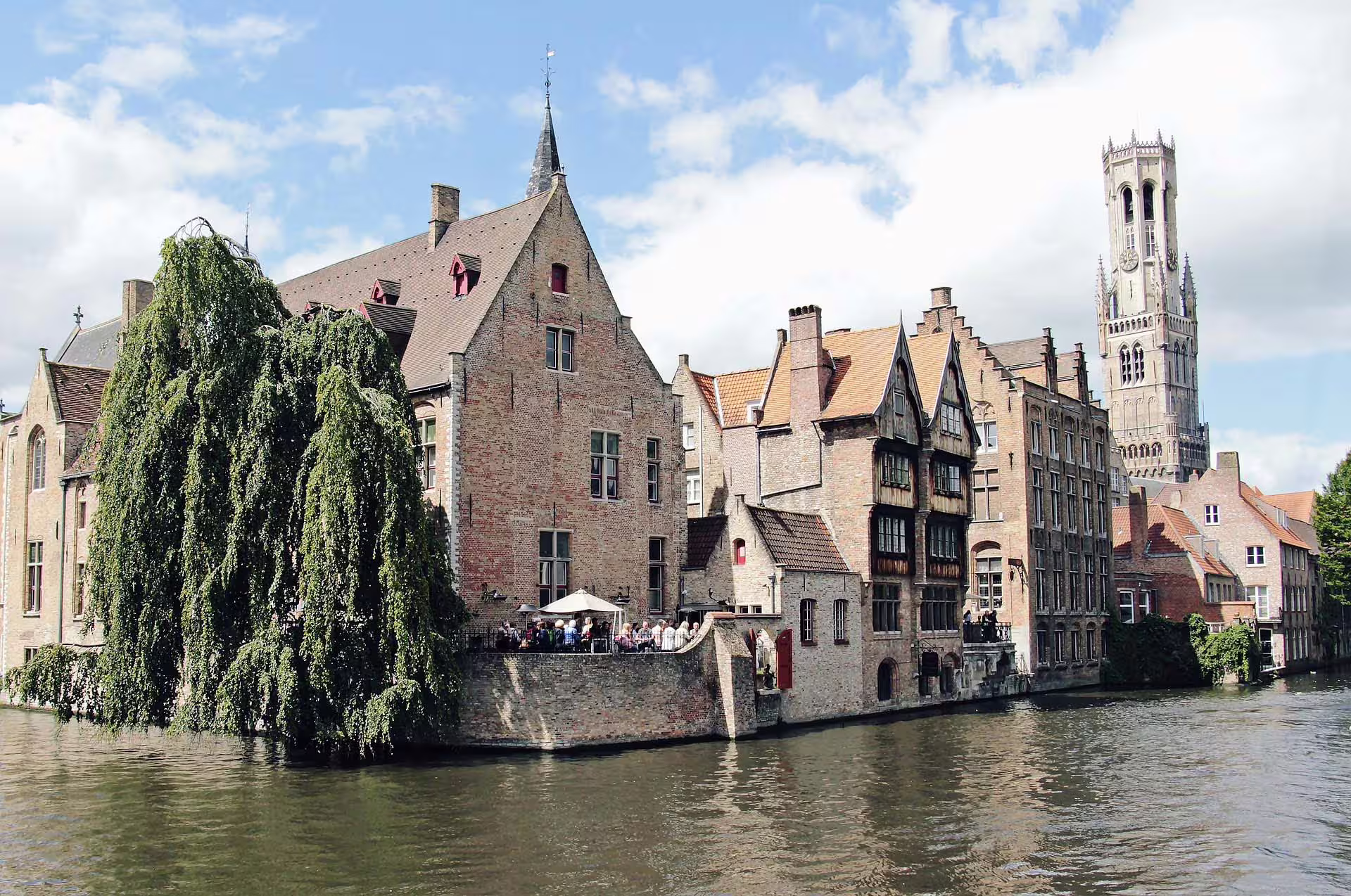 Scenic view of Bruges canal with historic Flemish architecture and iconic Belfry tower on a private walking tour in Flanders.