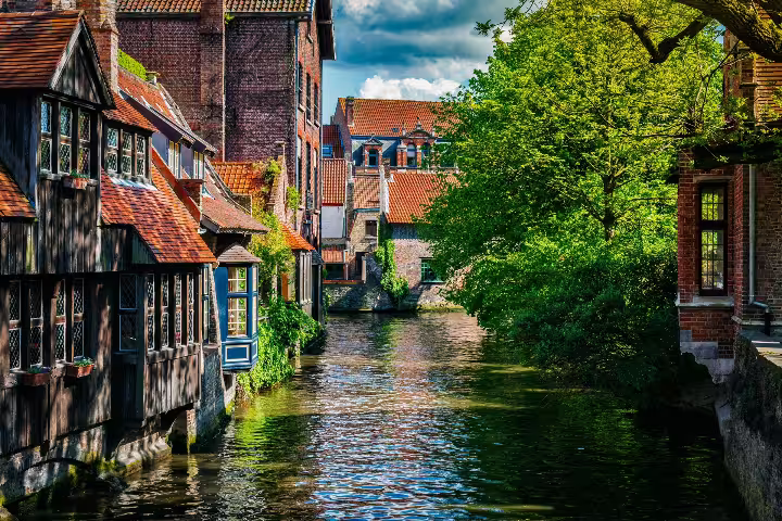Scenic canal view in Bruges, showcasing historic brick buildings and lush greenery on a private walking tour of Flanders.