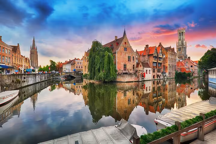 Bruges canal reflecting medieval brick buildings and Belfry tower at sunset