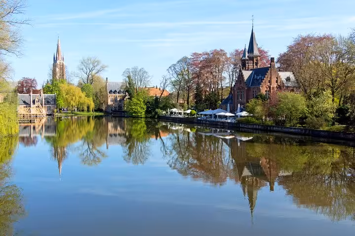 Tranquil canal reflecting medieval buildings and church spire among spring trees in Bruges