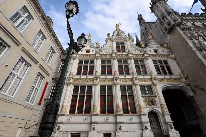 Ornate white Renaissance facade with golden details and red-trimmed windows in historic Bruges city center