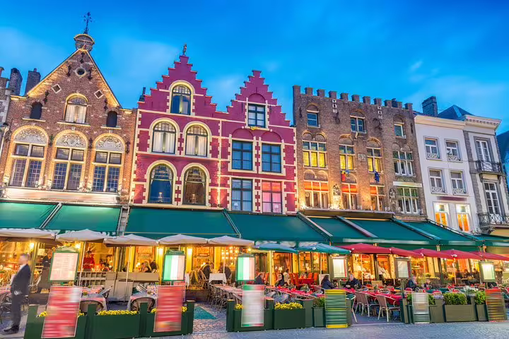 Bruges Market Square cafes and colorful guild houses at dusk on a guided day tour from Paris with hotel pick-up