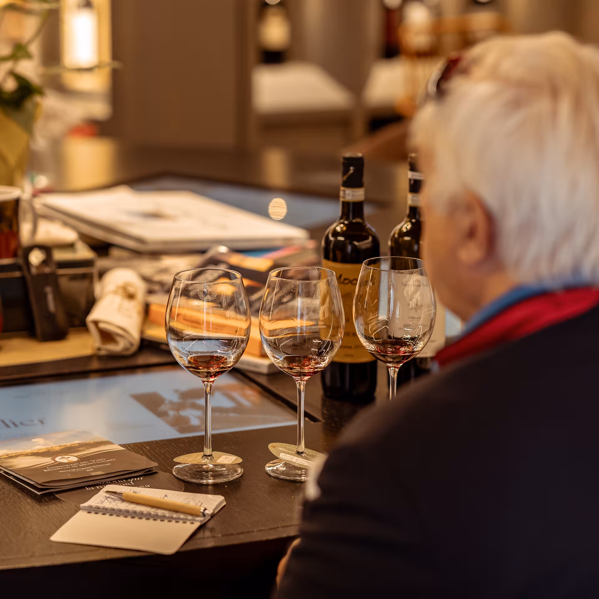 Wine enthusiast enjoying Brunello tasting session with three glasses and selection of brochures in Montalcino.
