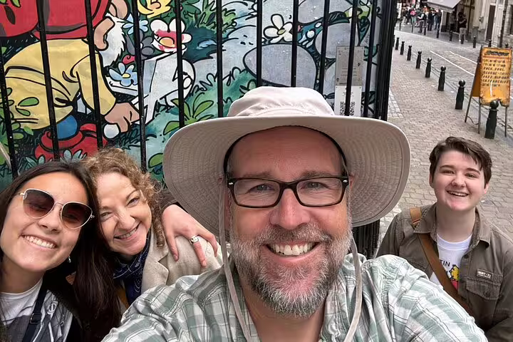 Group of four smiling tourists taking a selfie in front of a colorful comic strip mural gate in Brussels