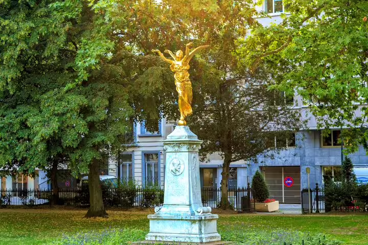 Golden winged statue on white pedestal in Brussels park surrounded by green trees