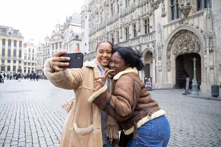 Tourists taking a selfie on a hidden gems walking tour in Brussels' historic Grand Place, capturing local culture and architecture.