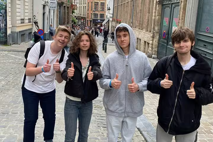 Four young tourists giving thumbs up on a cobblestone street in Brussels city centre