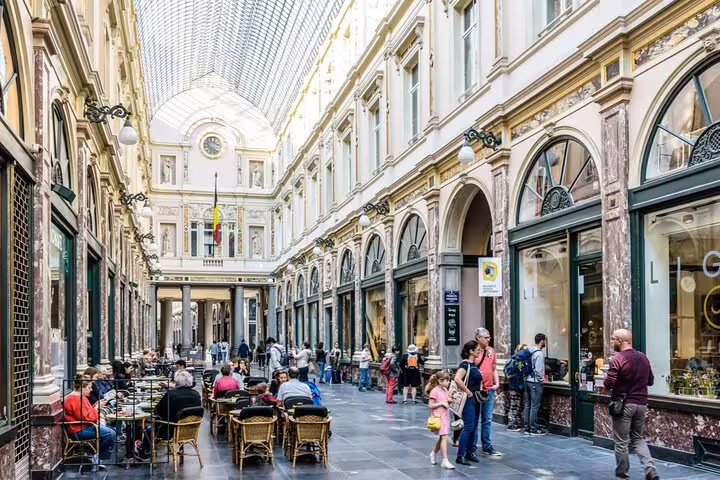 Elegant glass-roofed Royal Saint-Hubert Galleries in Brussels with tourists strolling past shops and cafés