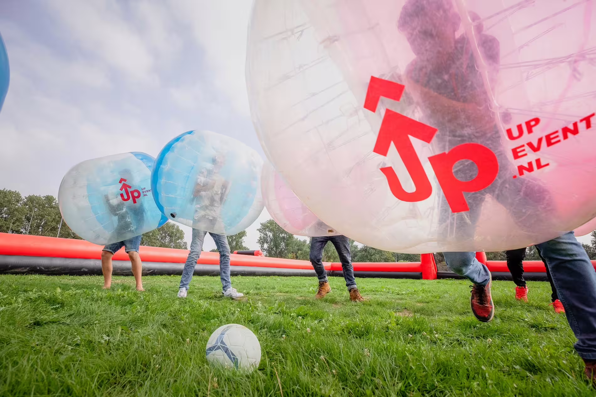 Players in inflatable bubbles chasing the ball during bubble football in Amsterdam on a grass pitch, team fun activity
