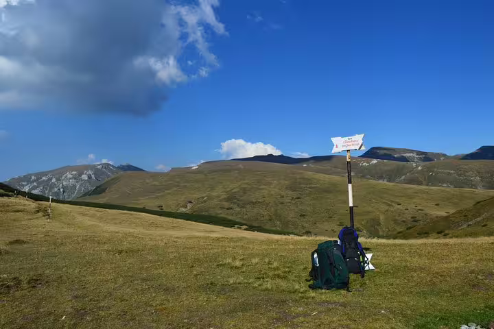 Hiking backpack resting at trail signpost in Bucegi Mountains with rolling green hills under blue sky