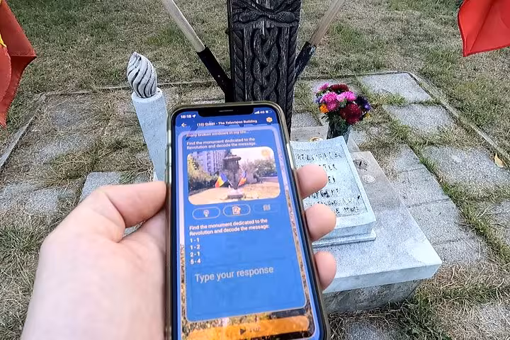 Visitor holding a phone with a quest clue near a 1989 Romanian Revolution memorial monument during a Bucharest walking tour