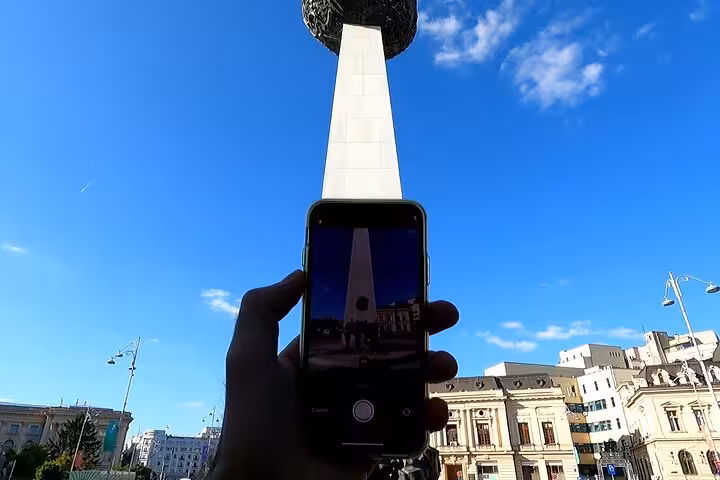 Tourist capturing Bucharest Revolution Memorial on smartphone during a self-guided 1989 walking tour in University Square.
