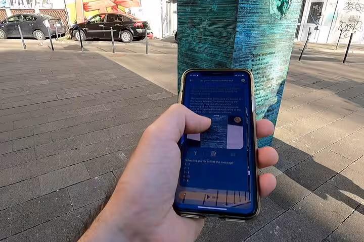 Traveler using a self-guided walking tour app near a graffiti-covered pillar on the Bucharest 1989 Revolution route.
