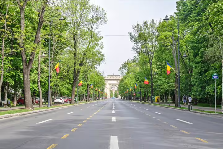 Tree-lined Kiseleff Boulevard in Bucharest with Romanian flags and triumphal arch in background