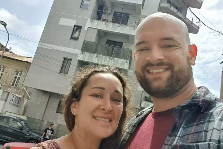 Smiling couple taking a selfie in front of a communist-era apartment block in Bucharest