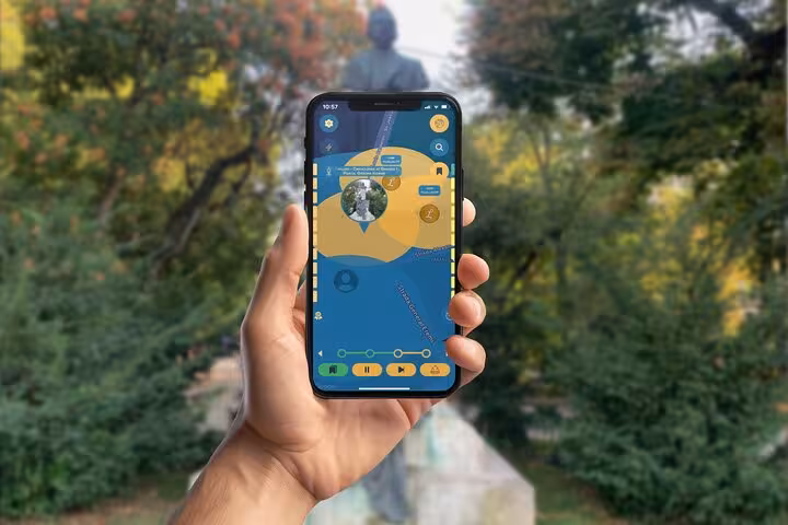 Hand holding smartphone with walking tour mobile app in front of a statue in Bucharest park