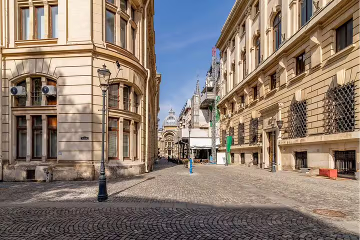 Cobblestone street in Bucharest Old Town lined with historic neoclassical buildings under blue sky