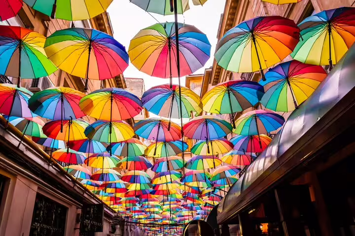 Colorful rainbow umbrellas suspended overhead along a narrow street in Bucharest Old Town