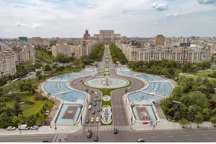 Aerial view of Bucharest city center with fountains, tree-lined boulevard, and Parliament Palace in background