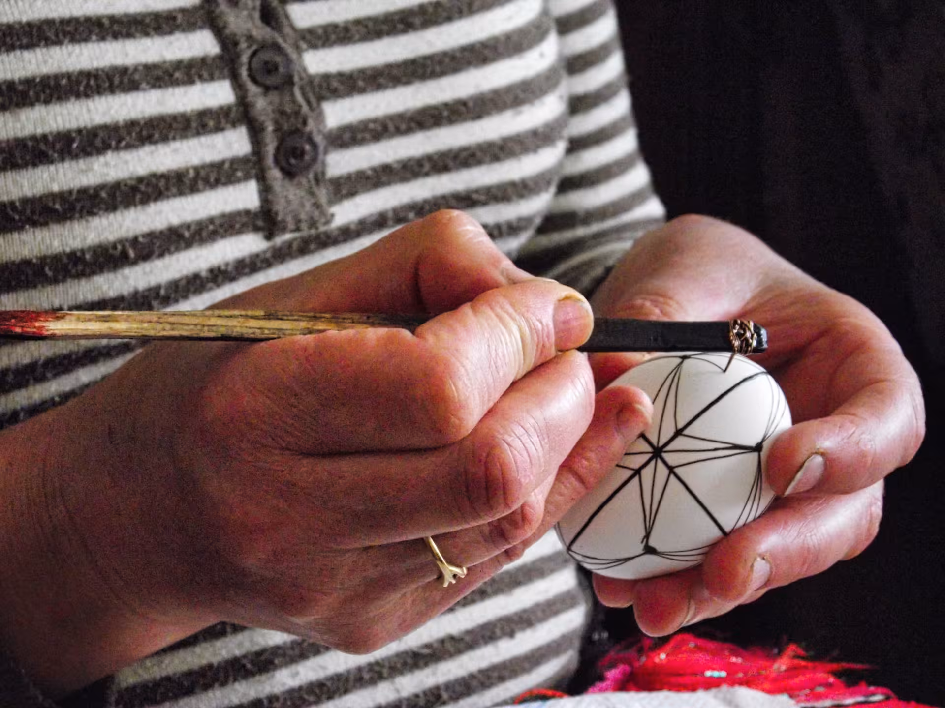 Artisan hands carefully painting intricate geometric patterns on a white Easter egg during Bucovina tour