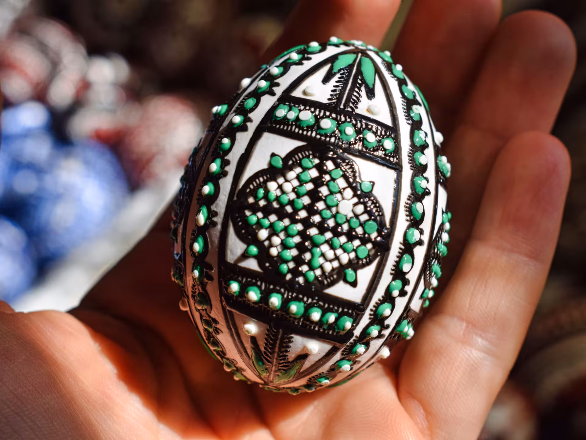 Hand-painted Bucovina Easter egg with intricate green and black traditional patterns held in palm