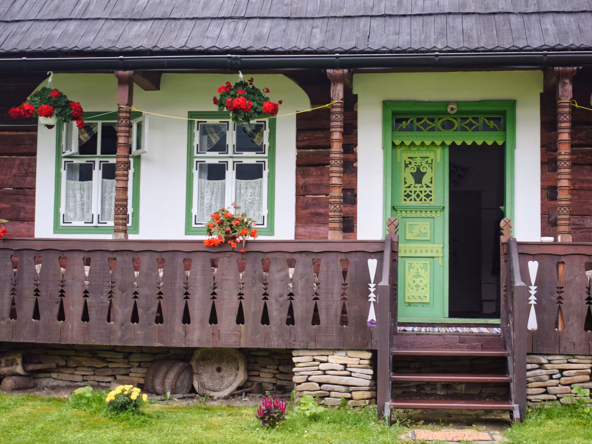 Traditional Romanian wooden farmhouse with carved green door and red geraniums in Bucovina village tour