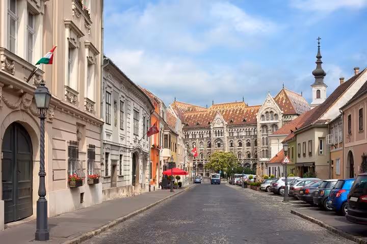 Cobblestone street in Buda Castle district with historic baroque buildings and ornate church spire, Budapest