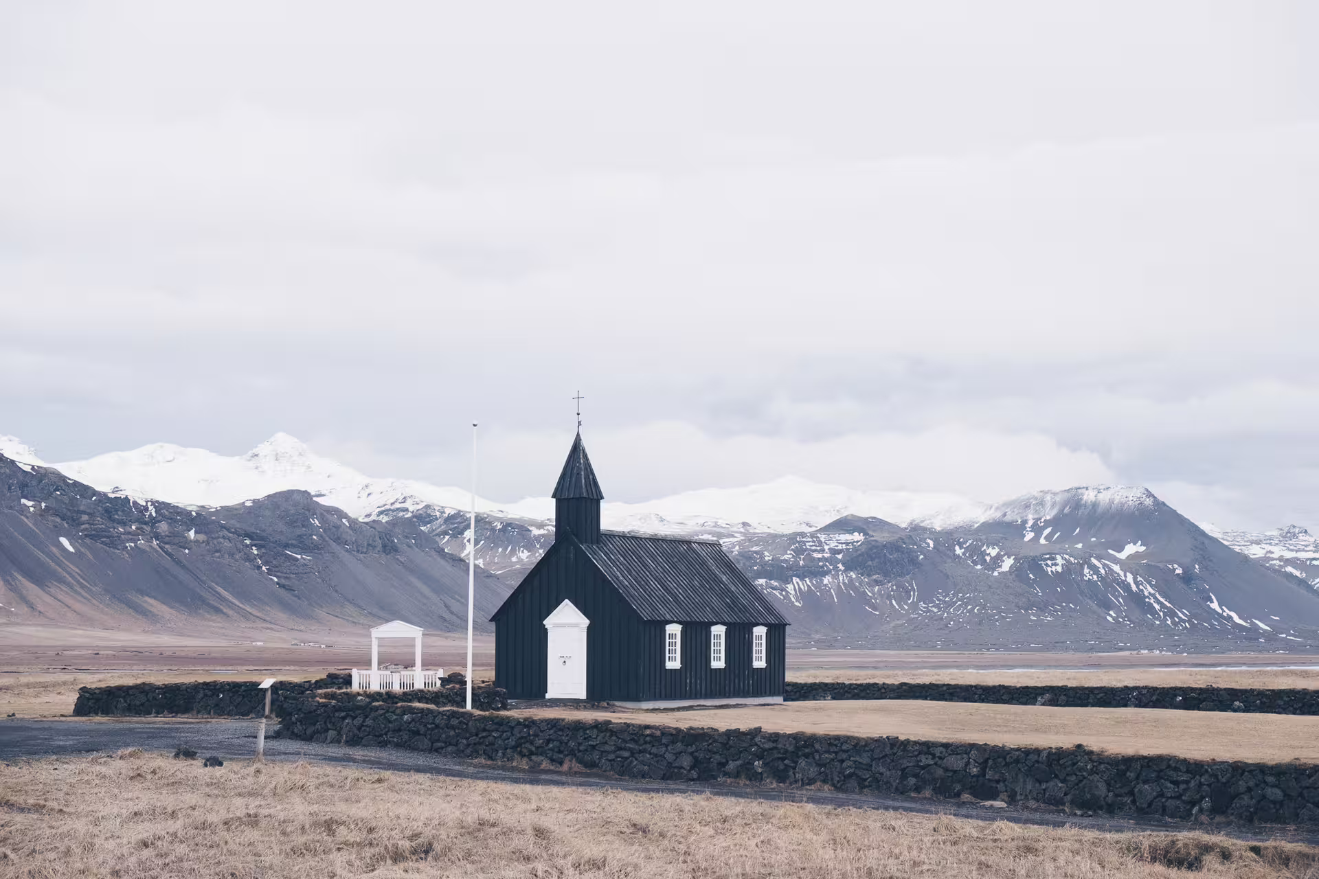 Black wooden church with white door and steeple surrounded by lava stone wall on Snaefellsnes Peninsula, Iceland