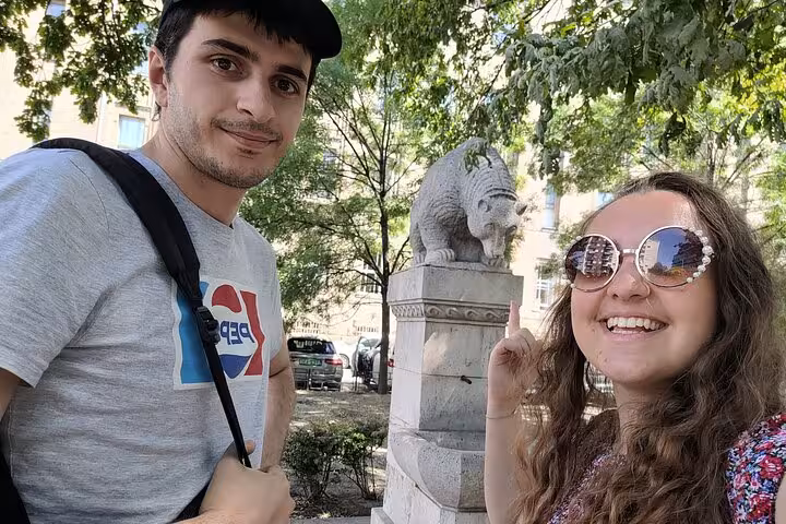 Two tourists posing with a stone lion statue during a self-guided walking tour in Budapest