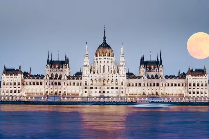 Hungarian Parliament Building illuminated at night reflecting on the Danube River with a full moon in Budapest
