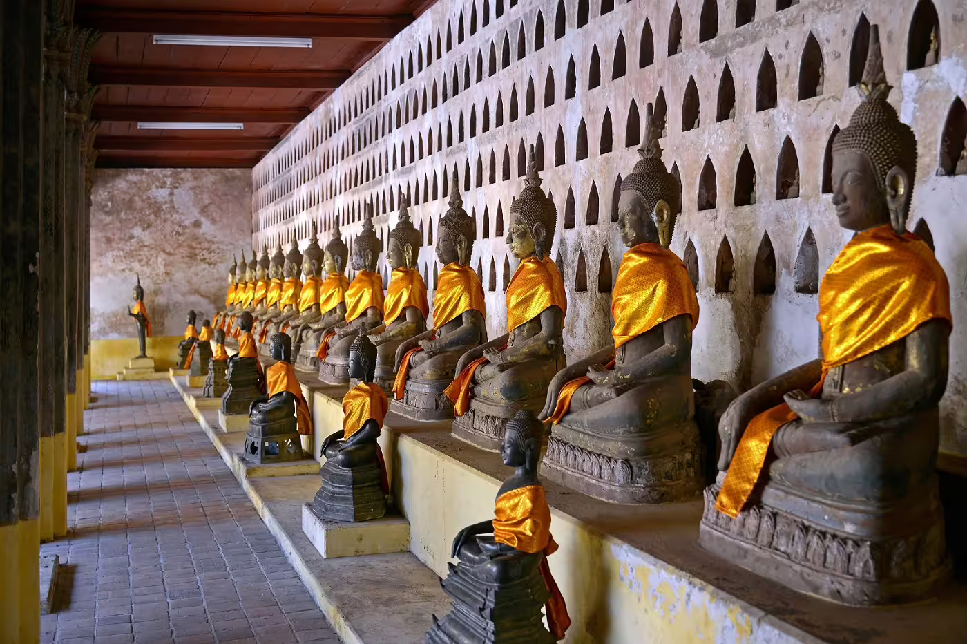 Row of serene Buddha statues draped in orange robes inside a historic temple in Laos, reflecting spiritual heritage.